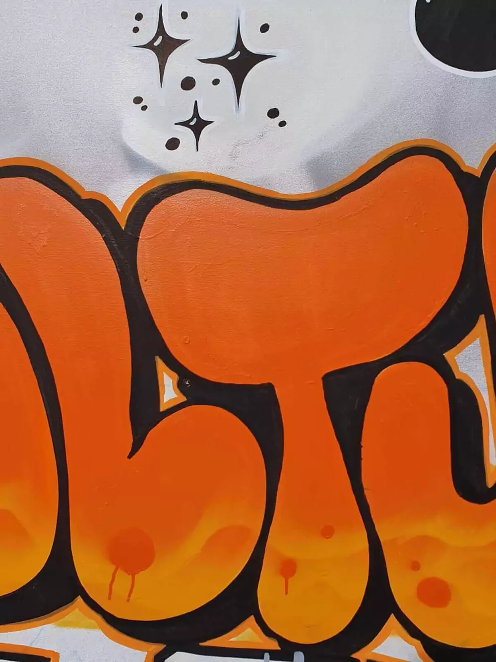 Gros plan sur le lettering orange de la fresque murale, bubble letters et motifs étoiles peints à la main
